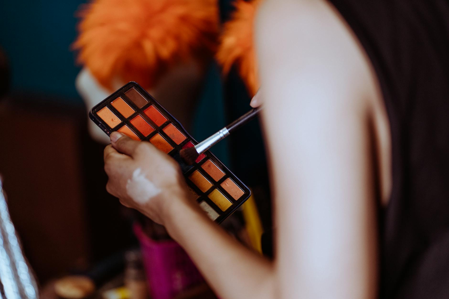 Crop ethnic anonymous visagiste putting eyeshadow with brush while creating makeup in studio