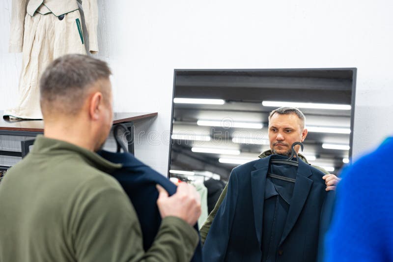 Person browsing stylish secondhand clothing at a thrift store and holding up a designer-look blazer