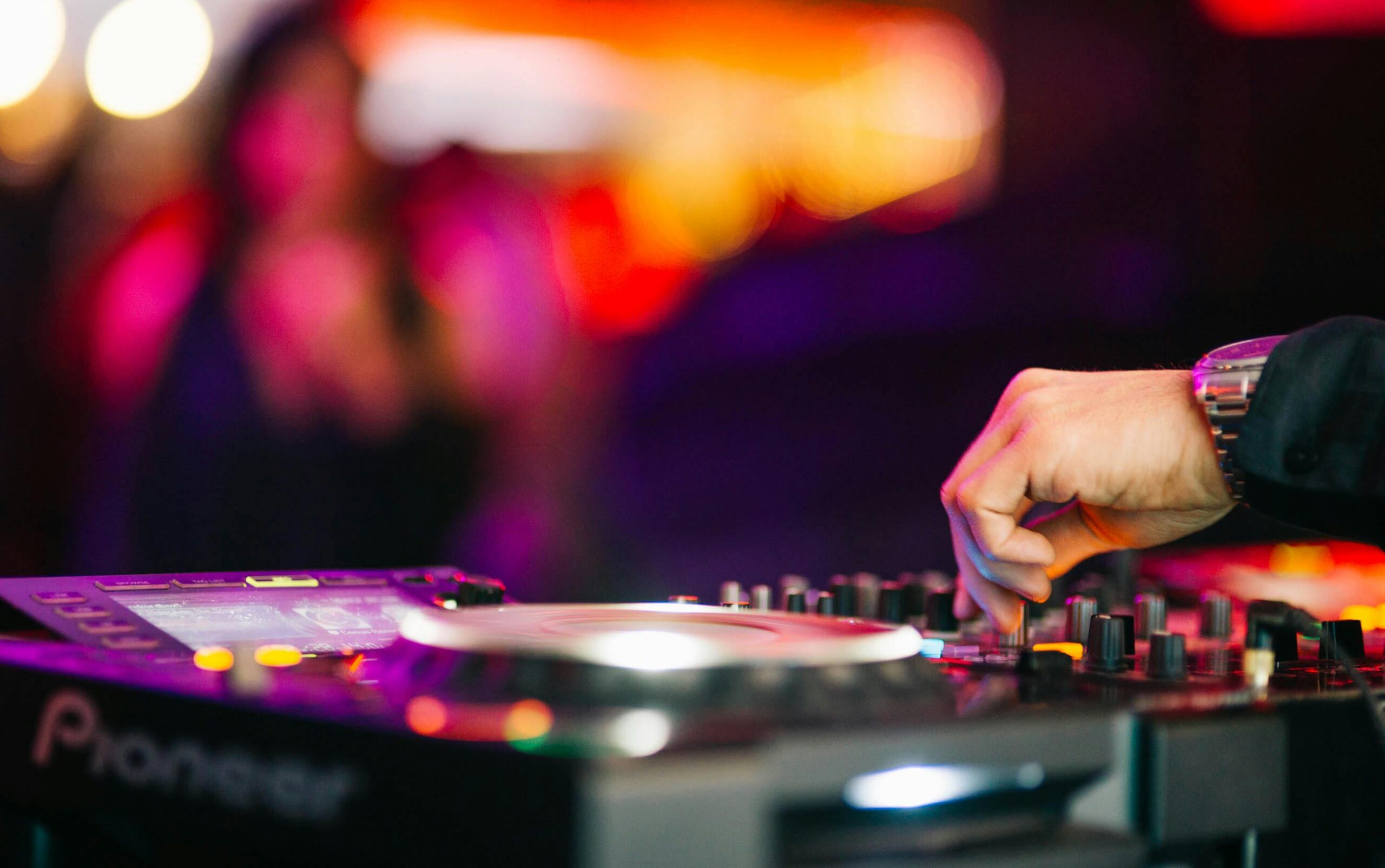 DJ's hands on Pioneer CDJ mixing equipment with nightclub dance floor in background
