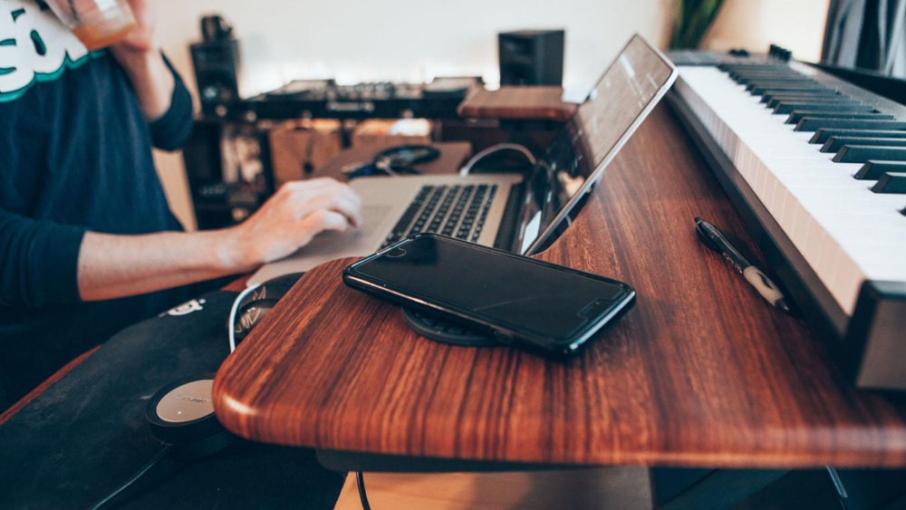Songwriter reviewing royalty payment dashboard on laptop while sitting at a piano in a home studio